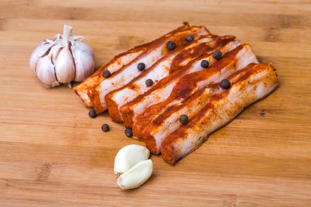Photo closeup traditional ukrainian preserved salted spicy red pepper lard bacon pork fat slices with garlic and allspice berries on wooden cutting board on timber background, horizontal pictureの写真素材