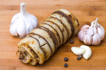 Photo closeup traditional ukrainian preserved salted spicy pepper rolled lard bacon pork fat with garlic and allspice berries on wooden cutting board on timber background, horizontal pictureの写真素材