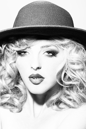 Portrait of one beautiful sensual sexy young retro blonde woman with curly hair and bright makeup in round hat looking forward in studio black and white, vertical pictureの写真素材