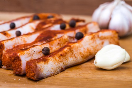 Photo closeup traditional ukrainian preserved salted spicy red pepper lard bacon pork fat slices with garlic allspice berries on wooden cutting board on blurred timber background, horizontal pictureの写真素材