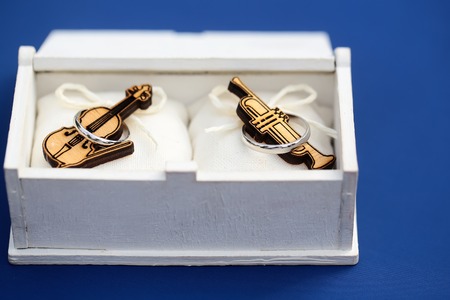 Closeup view of small wooden musical instrument of violin and saxophone lying in white box with silver ring on blue background, horizontal pictureの写真素材