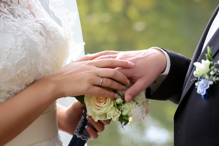 Closeup view of wedding young beautiful tender couple holding hands changing golden engagement rings with rose flowers bouquet outdoor, horizontal pictureの写真素材
