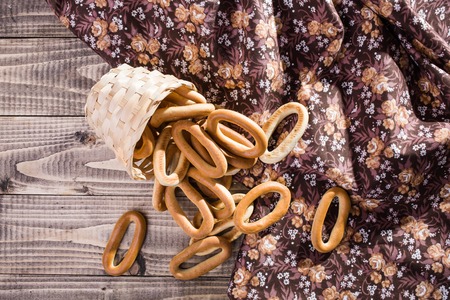 Photo top distant view still life basket lying sidelong with delicious hard oval cracknels poured out on wooden table near flowery cloth over sunny rustic background, horizontal pictureの写真素材