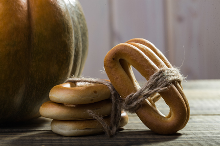 Photo closeup rustic autumn still life partial fresh orange pumpkin with bunches of hard oval cracknels bind with string on wooden table on timber background, horizontal pictureの写真素材