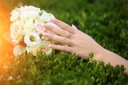Closeup view of one big round beautiful fresh wedding bouquet of rose flowers pink white and yellow pastel colors lying on green grass sunny day outdoor with female hand, horizontal pictureの写真素材