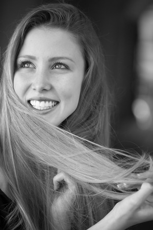 Closeup portrait of one beautiful happy smiling blonde young woman with long hair outdoor looking away on blurred background black and white, vertical pictureの写真素材