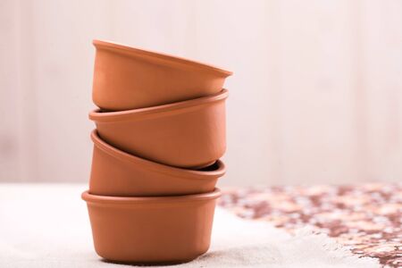Beautiful new empty round pottery stacked bowls dishware for cookery standing on table with white and floral tablecloth indoor on blur beige background, horizontal pictureの写真素材