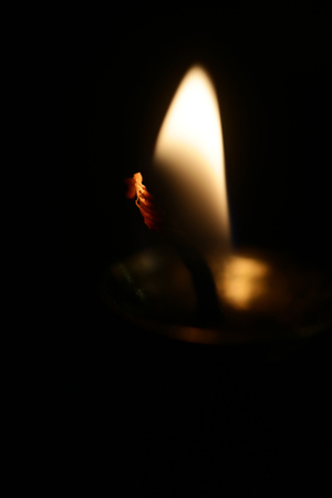 Photo closeup of single blurred soft warm flame of lighted fuse burning candlewick illuminating darkness on dark background, vertical pictureの写真素材