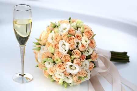 Photo front view side-on ball-shaped elegant wedding bouquet of fresh pastel pink white roses flowers with ribbons for bridal ceremony champagne glass on white indoor background, horizontal pictureの写真素材