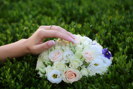 Closeup view of one big round beautiful fresh wedding bouquet of rose flowers pink white and yellow pastel colors lying on green grass sunny day outdoor with female hand, horizontal pictureの写真素材