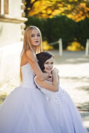 Pretty young blond woman with long hair and cute little girl with curly dark hair in white beautiful gowns hugging outdoor, vertical photoの写真素材