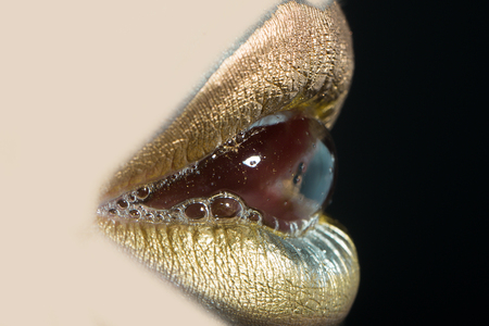 Closeup side view of sexual beautiful female open golden lips with bubble isolated on black background, horizontal pictureの写真素材