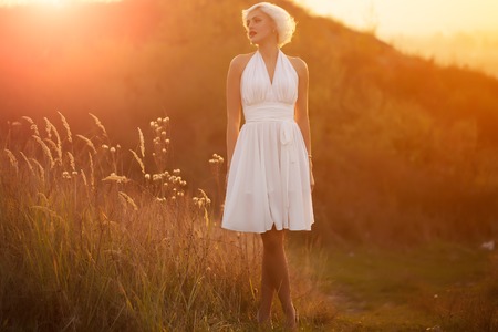 Full length view of one young beautiful fashionable retro sexy woman with blonde hair in white dress walking outdoor in sundown on natural background, horizontal pictureの写真素材
