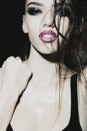 Closeup portrait of one beautiful young sexual woman with long wet curly hair and bright makeup looking forward indoor on studio background, vertical pictureの写真素材