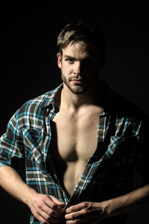 Closeup portrait of one handsome serious young sexy stylish man with beautiful muscular chest in checkered shirt looking forward in studio on black background, vertical pictureの写真素材