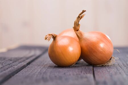 Rural autumn harvest vibrant raw ripe golden onions with husk laying on wooden table vegetables having sweet and aromatic savour indoor on light blur background closeup, horizontal pictureの写真素材
