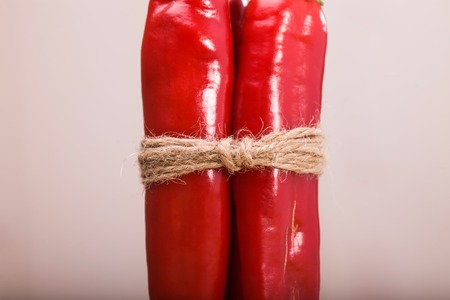 Bunch of two glossy red burning peppers cayenne vegetable tied by brown cord organic ingredient for piquant flavour in mexican food indoor on light background closeup, horizontal pictureの写真素材