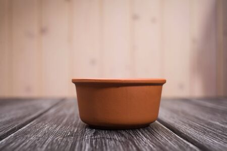 One beautiful clean pottery round ceramic terracotta color bowl standing on wooden table on light blur background closeup studio copyspace, horizontal pictureの写真素材