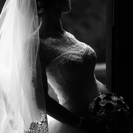 Photo closeup of beautiful young bride in ornamental wedding lace dress long veil holding elegant bouquet of fresh flowers for bridal ceremony black and white on grey background, square pictureの写真素材