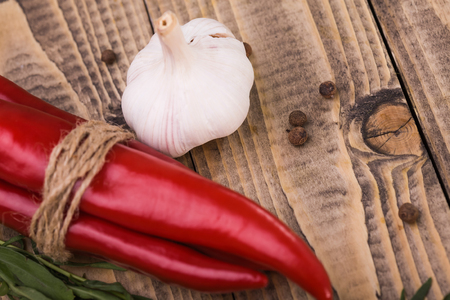 Beautiful ripe raw shining bright red hot chili peppers tied by rope white aromatic garlic some allspice vegetables rustic natural condiment eco product closeup on wooden background studio, horizontalの写真素材