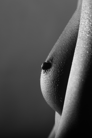 Closeup side view of one female beautiful bare chest with nipple and soft skin of young adult woman in studio black and white, vertical pictureの写真素材