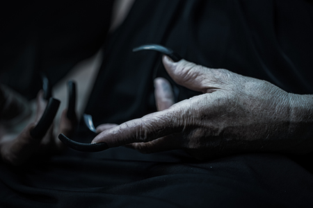 Photo closeup of female hands of old woman with aged wrinkled skin and polished long parrot-beak fingernails black and white on dark blurred background, horizontal pictureの写真素材