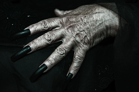 Photo closeup of female hand of old woman with aged wrinkled skin and polished long parrot-beak fingernails black and white lying on dark mourning blurred tulle background, horizontal pictureの写真素材