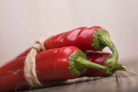 Vegetarian natural fiery ingredient condiment ripe red poignant cayenne pepper vegetable tied by rope lying on wooden table indoor on light background closeup, horizontal pictureの写真素材