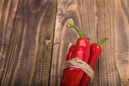 Bunch of red pungent chili peppers with green tails tied by rope natural eco ingredient on wooden background closeup copyspace, horizontal pictureの写真素材