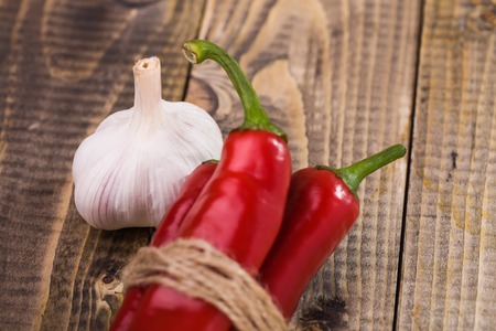 Closeup of appetizing organic aromatic spiciness ripe garlic and shining bright red chili peppers with green tails tied by brown rope healthy vegetarian diet on wooden background, horizontal pictureの写真素材
