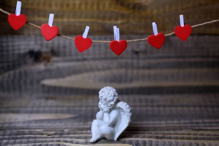 Closeup view of one beautiful cupid angel decorative figurine near red clothes-peg in shape of heart with no people on wooden background, horizontal pictureの写真素材