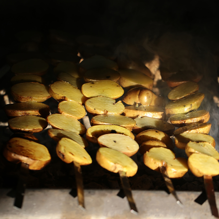 Photo closeup of delicious hot potatoes vegetables cooked on grill charbroiled barbecue on brazier on blurred smoky background, square pictureの写真素材