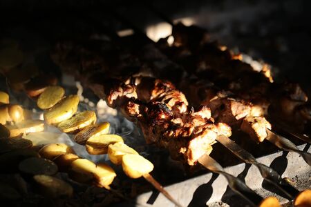 Photo closeup of delicious hot potatoes and meat skewers cooked on grill charbroiled barbecue on brazier on blurred smoky background, horizontal pictureの写真素材