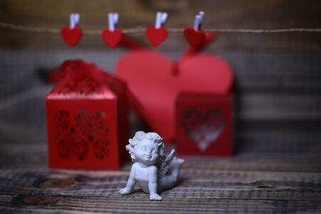 Closeup view of one beautiful cupid angel decorative figurine near red paper greeting valentine box...