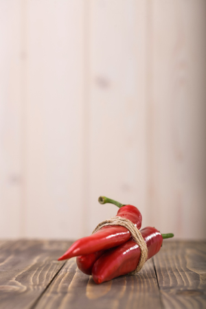 Three red fresh eating raw pod peppers cayenne vegetable tied by twine laying on wooden table on light background fiery seasoning for mexican food indoor copyspace closeup, vertical pictureの写真素材