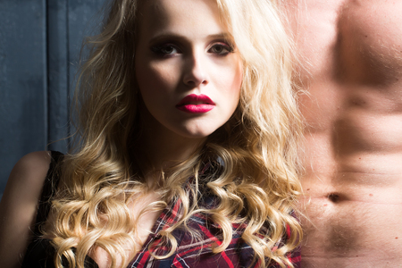 Young sexual attractive sensual couple of blonde woman with long curly hair and naked muscular man with beautiful body close to each other in studio on wooden background, horizontal pictureの写真素材