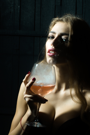Closeup view portrait of one beautiful young sensual serious enigmatic enchanted woman holding in hand drinking glass full of liquid with smoke of magic elixir of beuty and life and secret of youthの写真素材