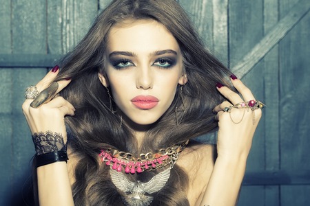 Pretty sensual glamour young fashionable girl with long curly hair bright makeup and many colorful different costume jewellery of necklace rings and earrings on wooden background, horizontal pictureの写真素材