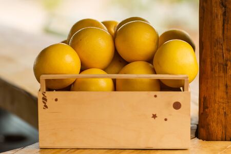 Closeup one timber lug-box full of clean organic natural fresh tasty ripe yellow grapefruits crop fruit full of vitamin for healthy eating diet on light blurred background, horizontal pictureの写真素材