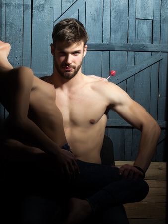 Young sexy sensual topless couple of woman with flexible beautiful body and bare chest sitting on handsome bearded man in jeans looking forward indoor on studio background, vertical pictureの写真素材