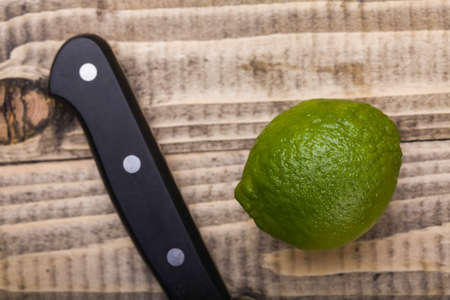 One whole fresh juicy green lime and knife with black handle on brown wooden table, horizontal photoの写真素材