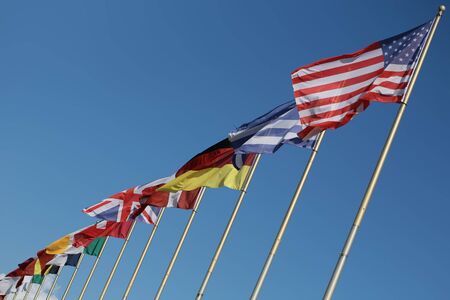 Photo long shot of different national flags flutter in wind on tall flagstaffs in rows against...