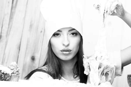 One beautiful young female cook in professional white uniform of hat and apron cooking homemade food...