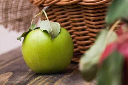 Closeup photo of whole fresh ripe juicy green apple with smooth peel and leaves on shank near basket...