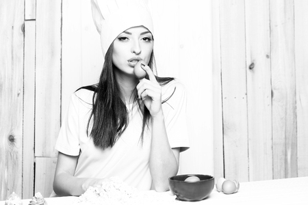 One beautiful young female cook in professional white uniform of hat and apron cooking homemade food making dough of flour and eggs in kitchen on wooden background, horizontal pictureの写真素材
