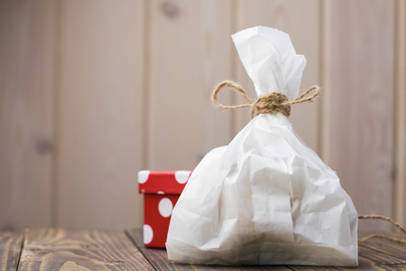 Full paper food sack with brown rope bow near small bright red with white dots handmade package holiday gift on wooden table indoor copyspace on light background, horizontal pictureの写真素材