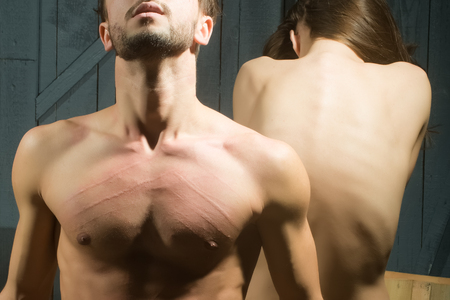 Young adult sensual couple of handsome man with fresh red score on bare chest from female nails and back view of beautiful straight naked woman indoor, horizontal pictureの写真素材