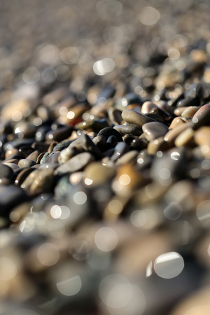 Photo blurred closeup large quantities of wet grey smooth fragments clasts of marine rubbles pebbles stones rocks of various sizes forms surface outdoor on shingle beach background, vertical pictureの写真素材