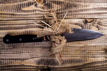 Cross shaped Halloween sackcloth voodoo doll pierced with sticks on chest lies on knife on brown...