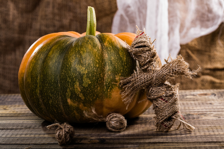Halloween concept of spooky rag doll with two clews of twine near big round pumpkin with green spot on wooden table on white and brown cloth background, horizontal photoの写真素材